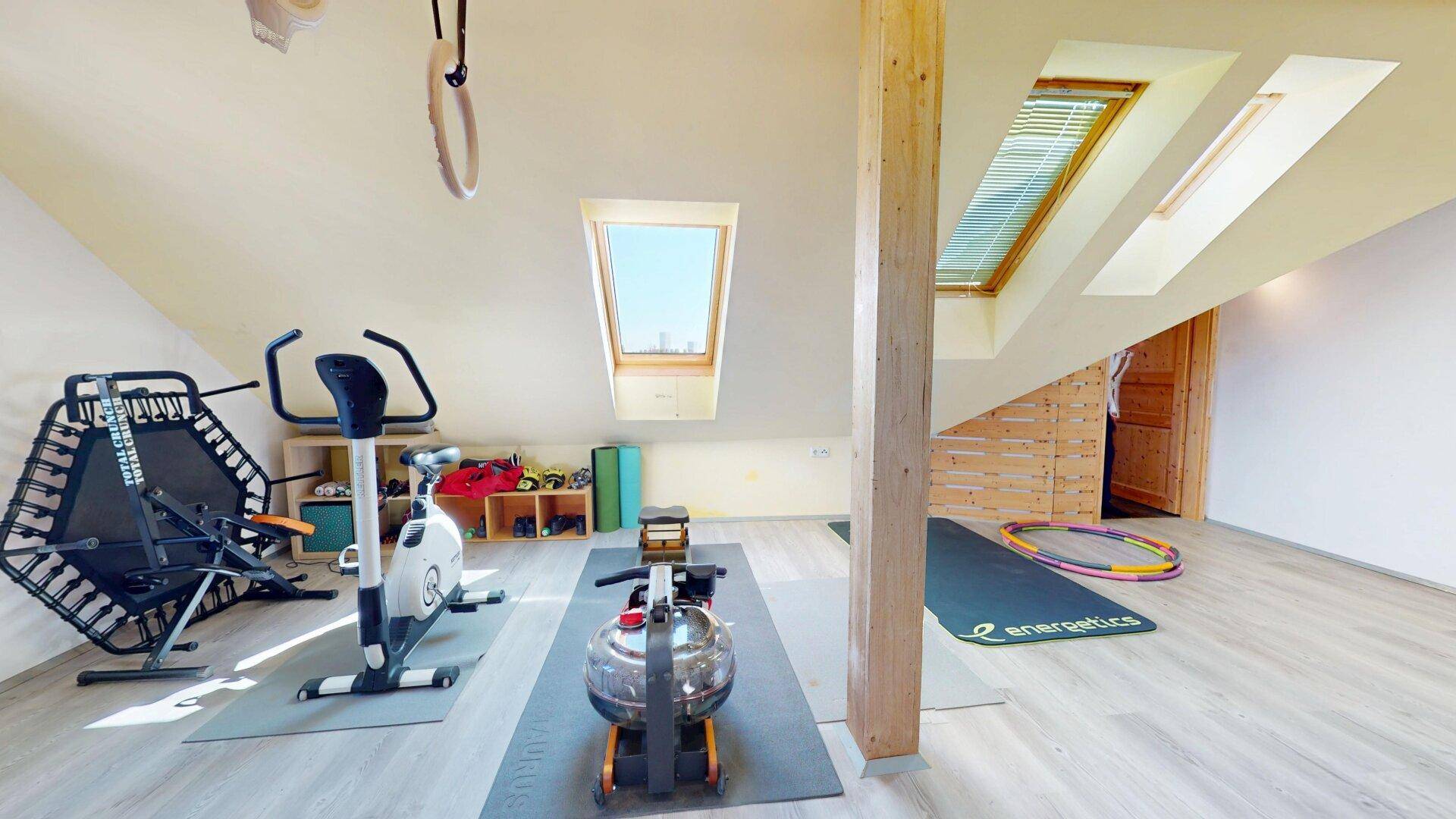 Geräumiger Fitnessraum im Dachgeschoss mit verschiedenen Trainingsgeräten und Dachfenstern.