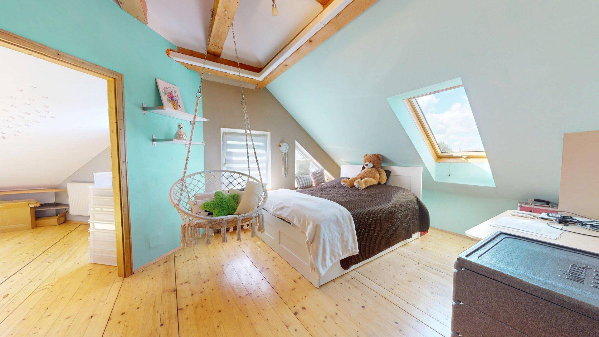 Kinderzimmer im Dachgeschoss mit Bett, Schaukel und Dachfenster, hell und freundlich gestaltet.