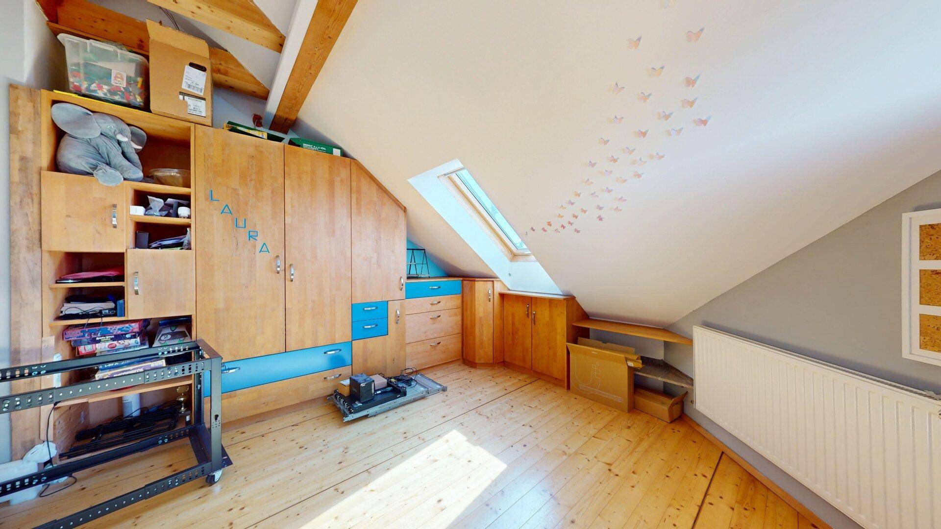 Kinderzimmer mit großem Holzschrank, Dachfenster und spielerischer Wanddekoration.