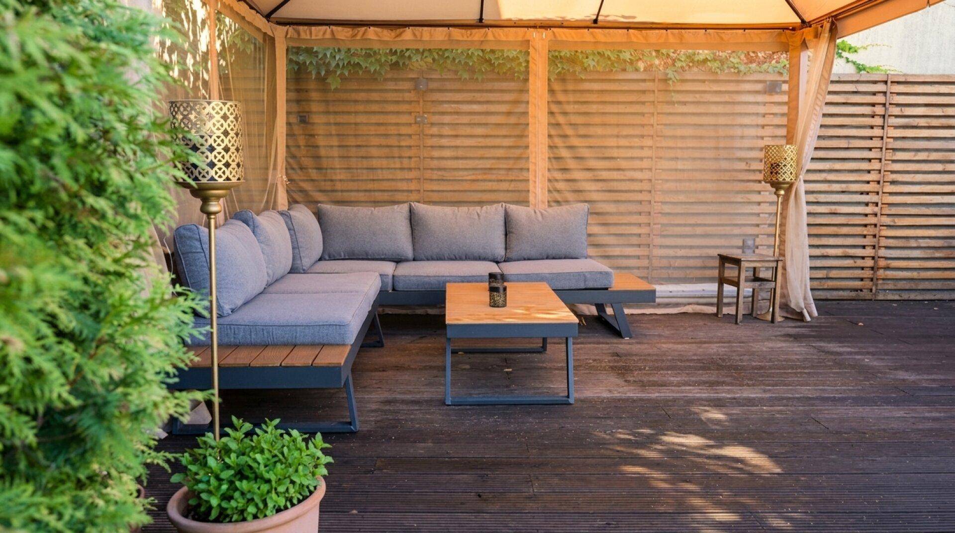 Moderner Lounge-Bereich im Freien unter einem Pavillon mit bequemen Sitzmöbeln auf einer Holzterrasse.