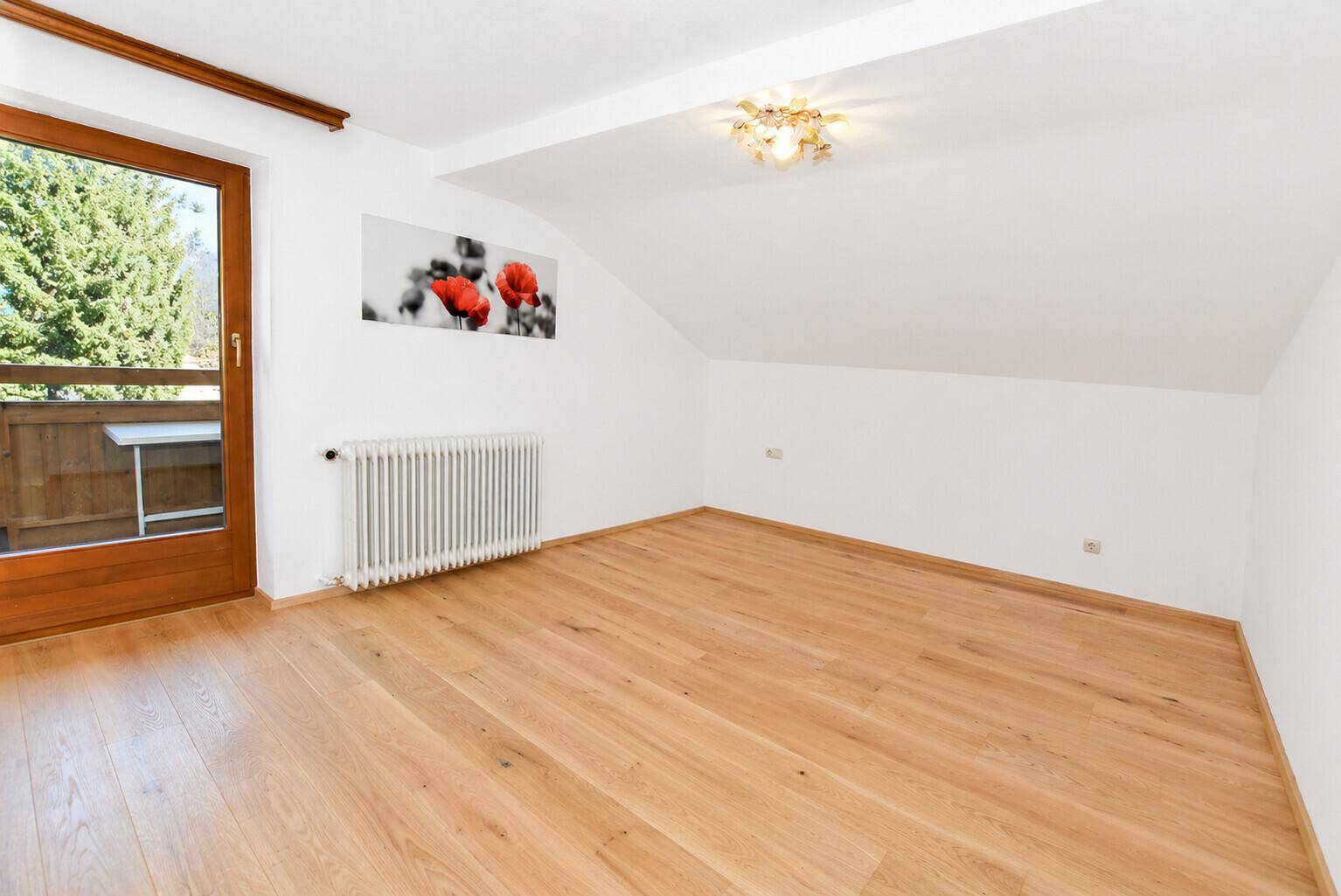 Geräumiges Zimmer mit Holzboden, Dachschräge und direktem Zugang zu einem sonnigen Balkon.