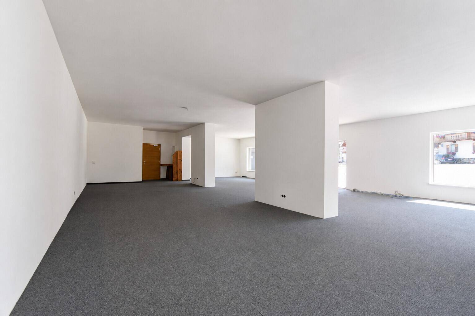 Weitläufiger, leerer Gewerberaum mit Säulen und Teppichboden, bereit für individuelle Einrichtung und Nutzung.