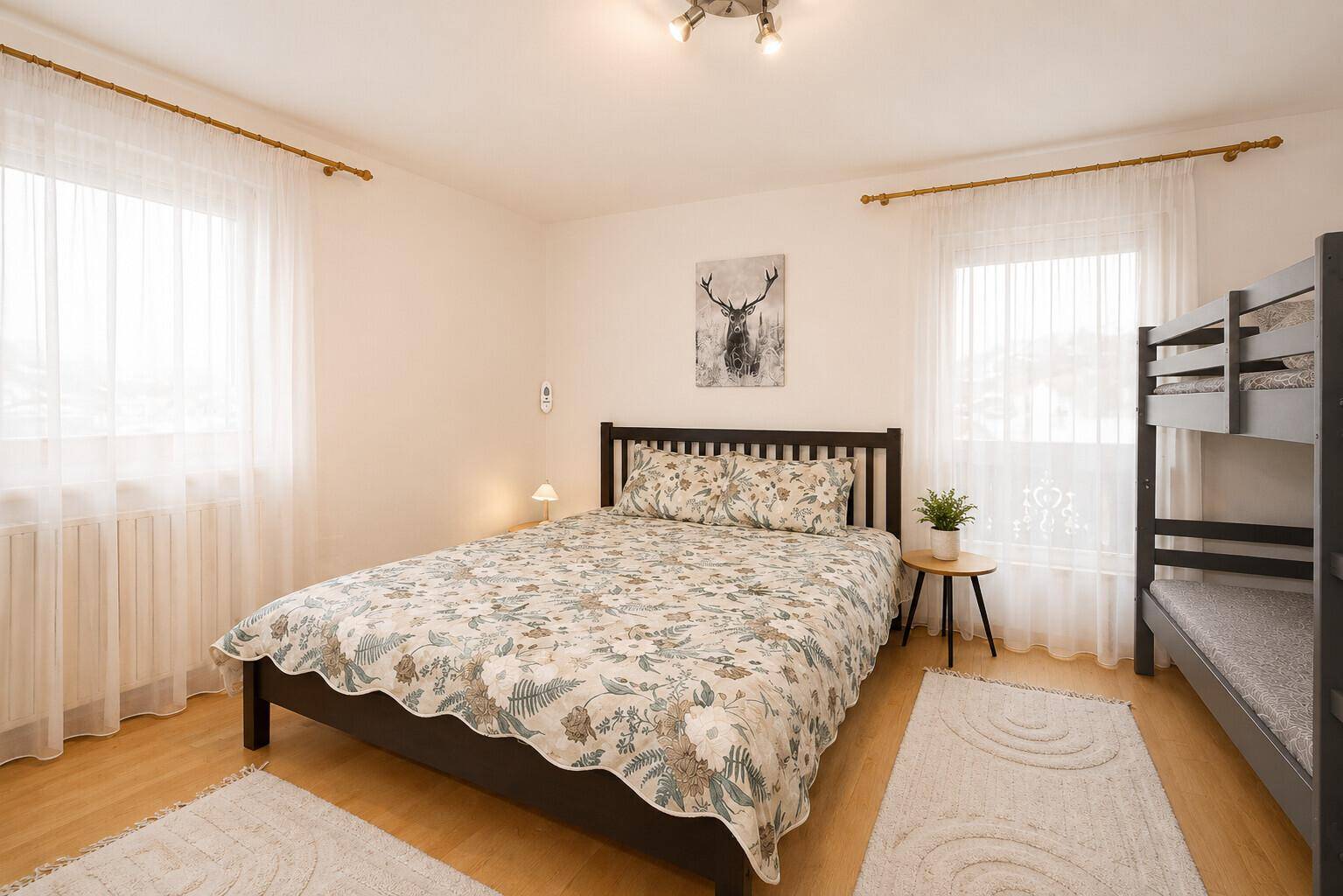 Geräumiges Schlafzimmer mit Doppelbett, Etagenbett und zwei Fenstern.