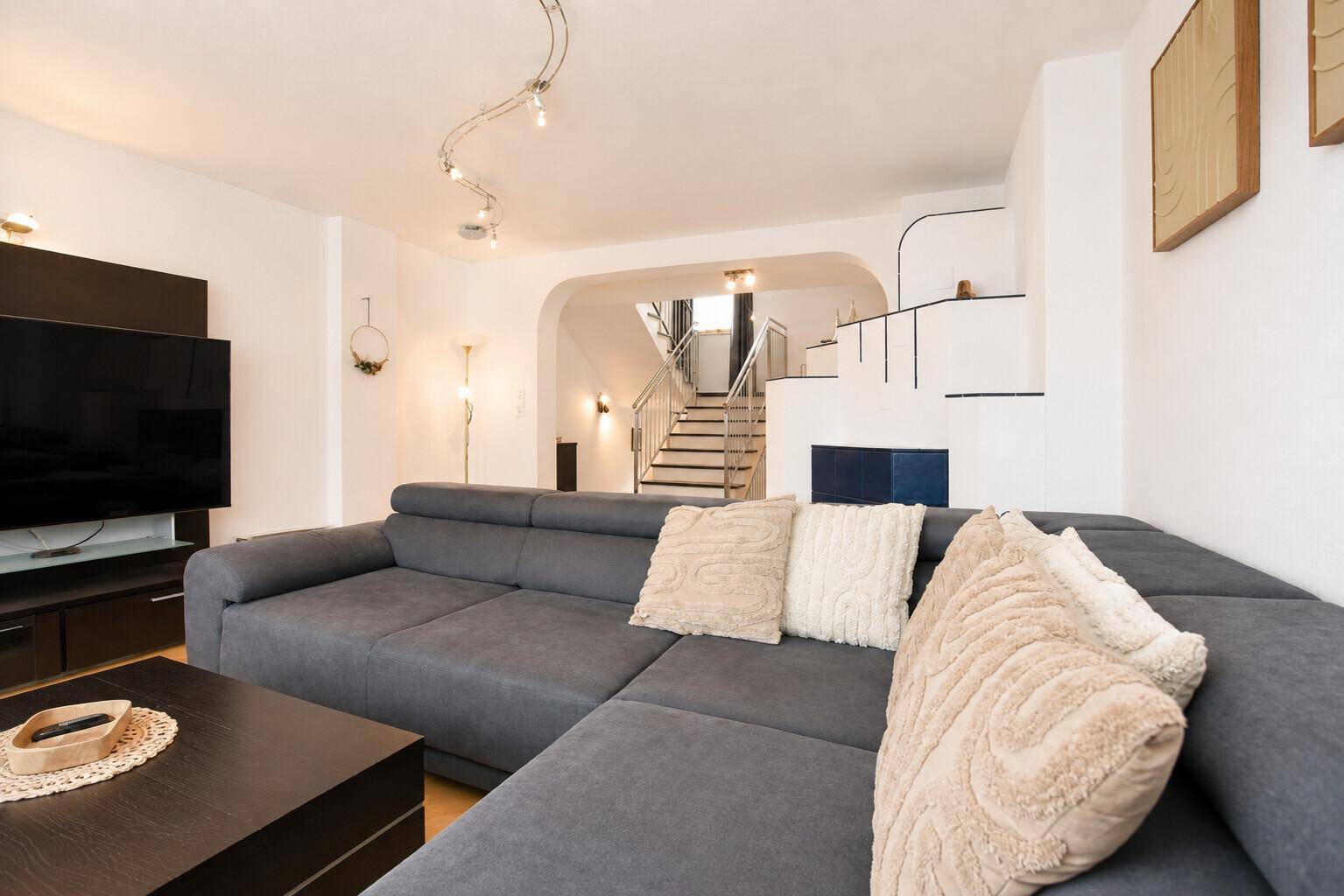Geräumiges Wohnzimmer mit großem Ecksofa, Fernseher und Blick auf die Treppe.