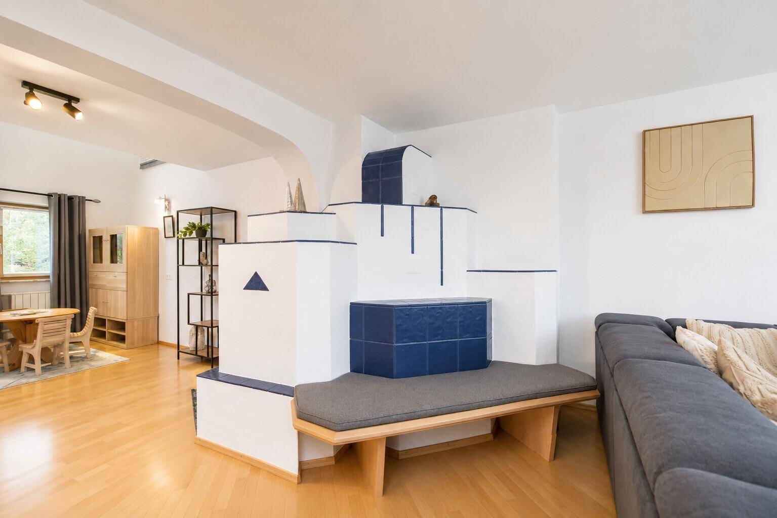 Helles Wohnzimmer mit modernem Kachelofen, Holzboden und gemütlichem Sofa.