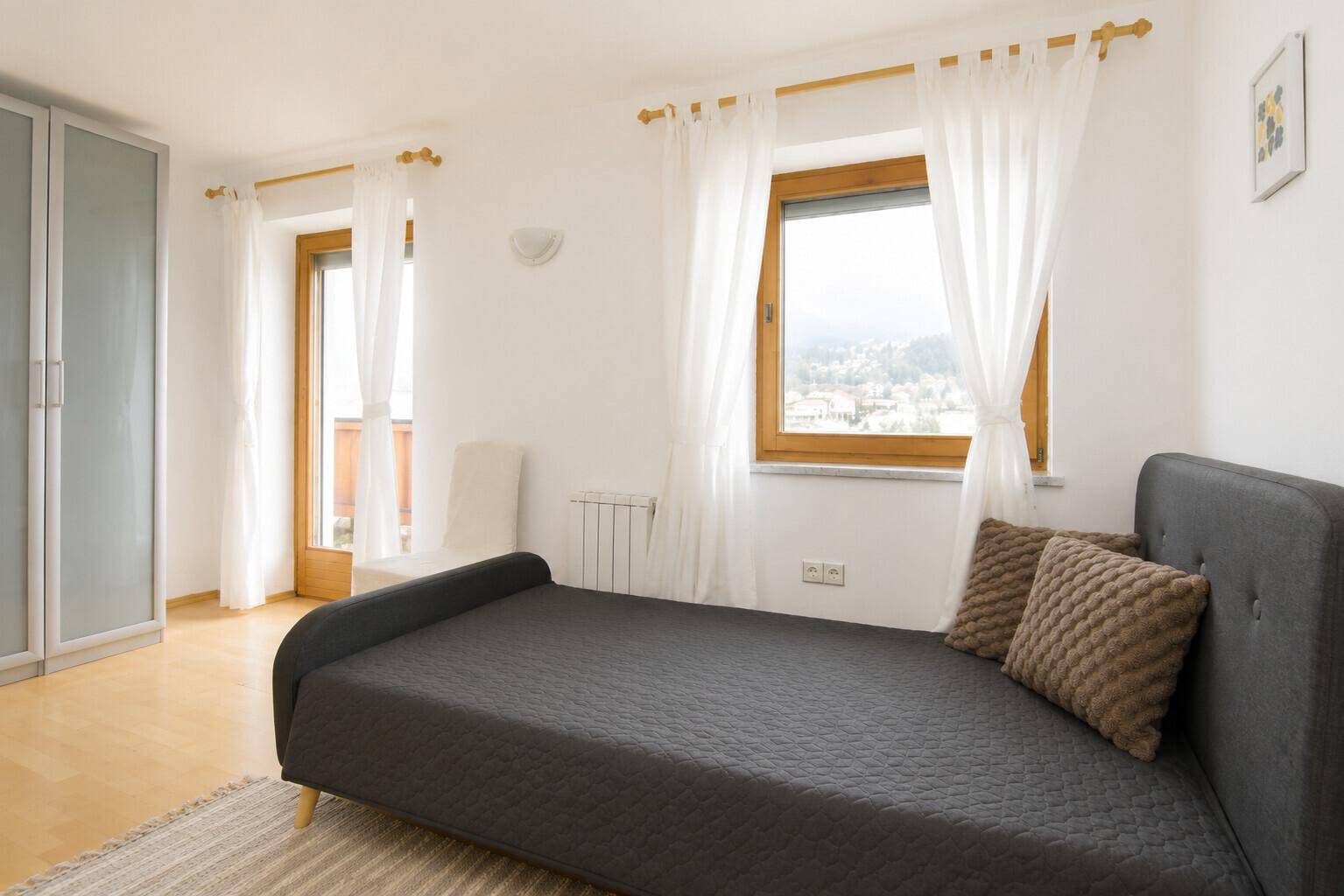 Gemütliches Schlafzimmer mit Einzelbett, Balkonzugang und hellem Holzboden.