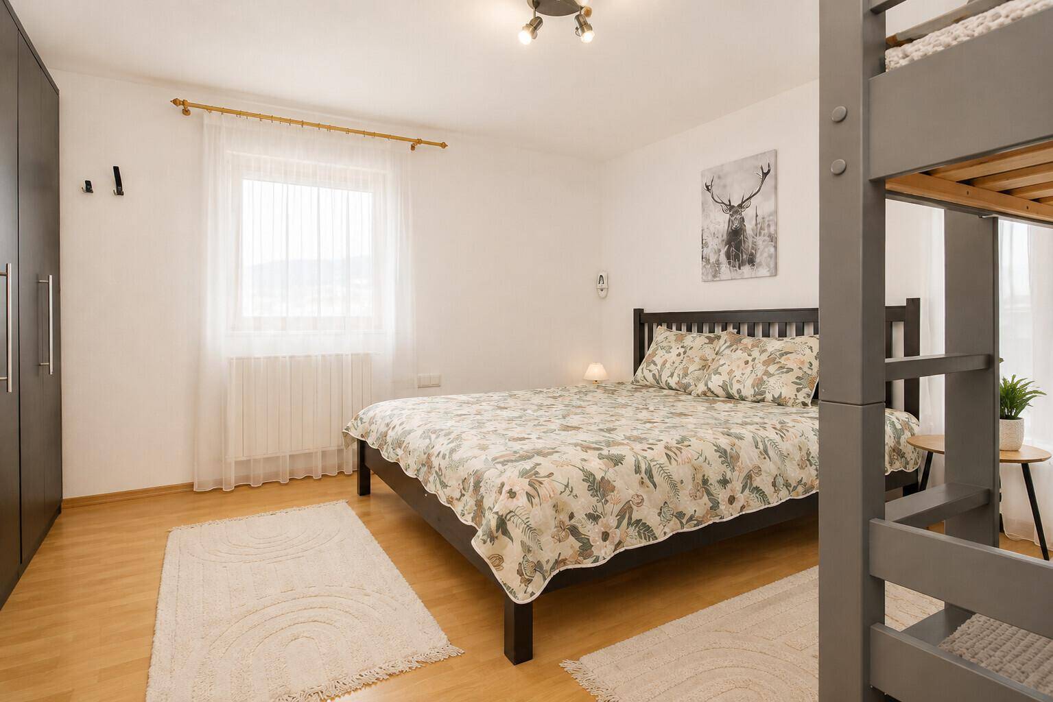 Helles Schlafzimmer mit Doppelbett, Etagenbett und Kleiderschrank.