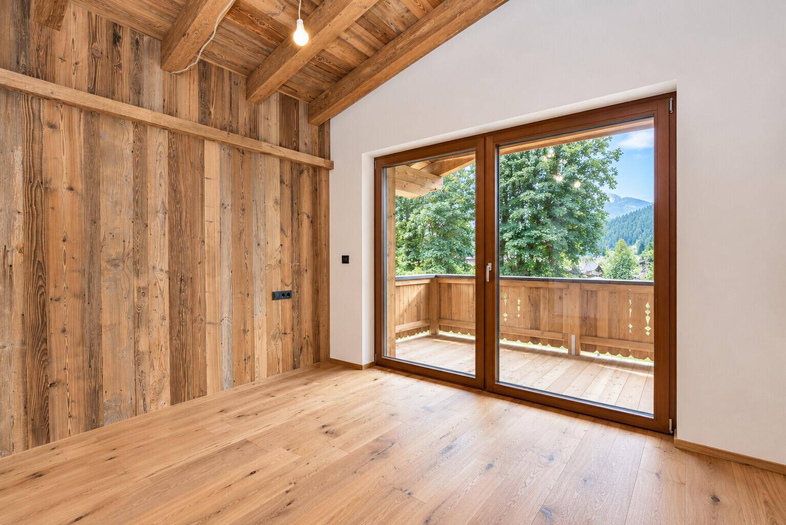 Gemütliches Schlafzimmer mit Holzwand, Holzboden und Balkonzugang mit Blick ins Grüne.