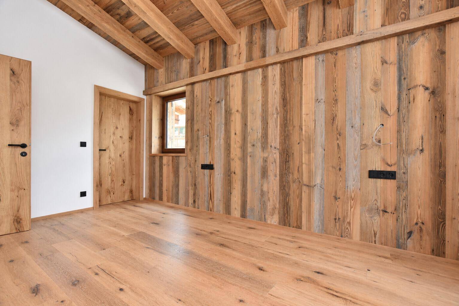 Schlafzimmer mit Holzboden, Holzwandverkleidung und Holztür in rustikalem Stil.