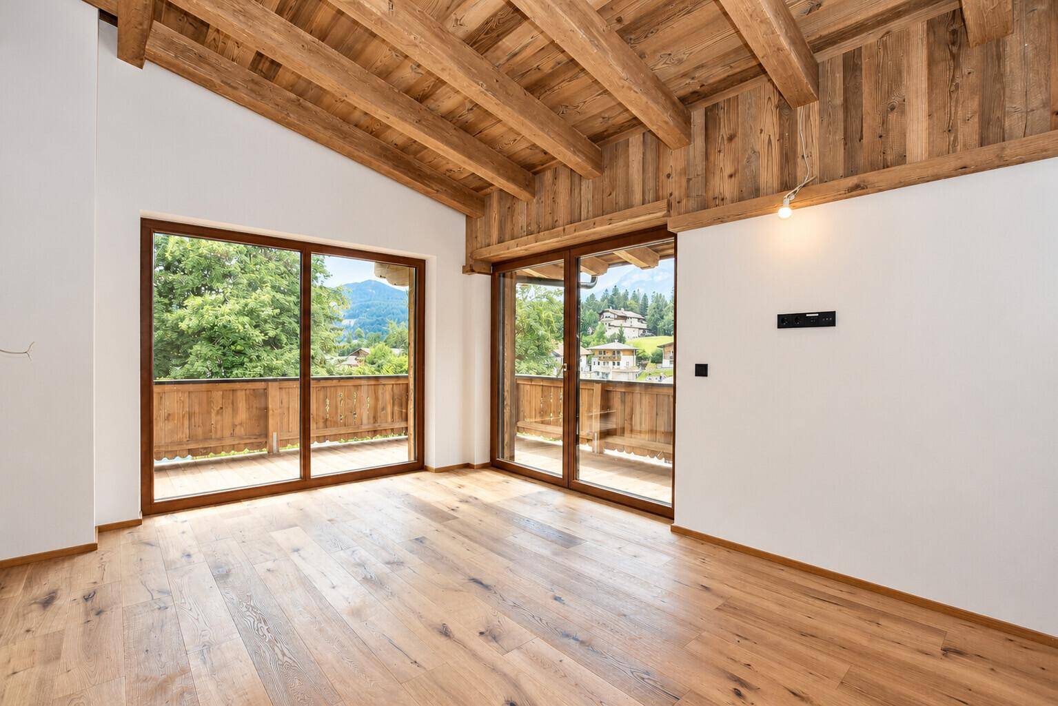Helles Schlafzimmer mit Holzbalkendecke, Holzboden und Zugang zu einem Balkon mit Bergblick.