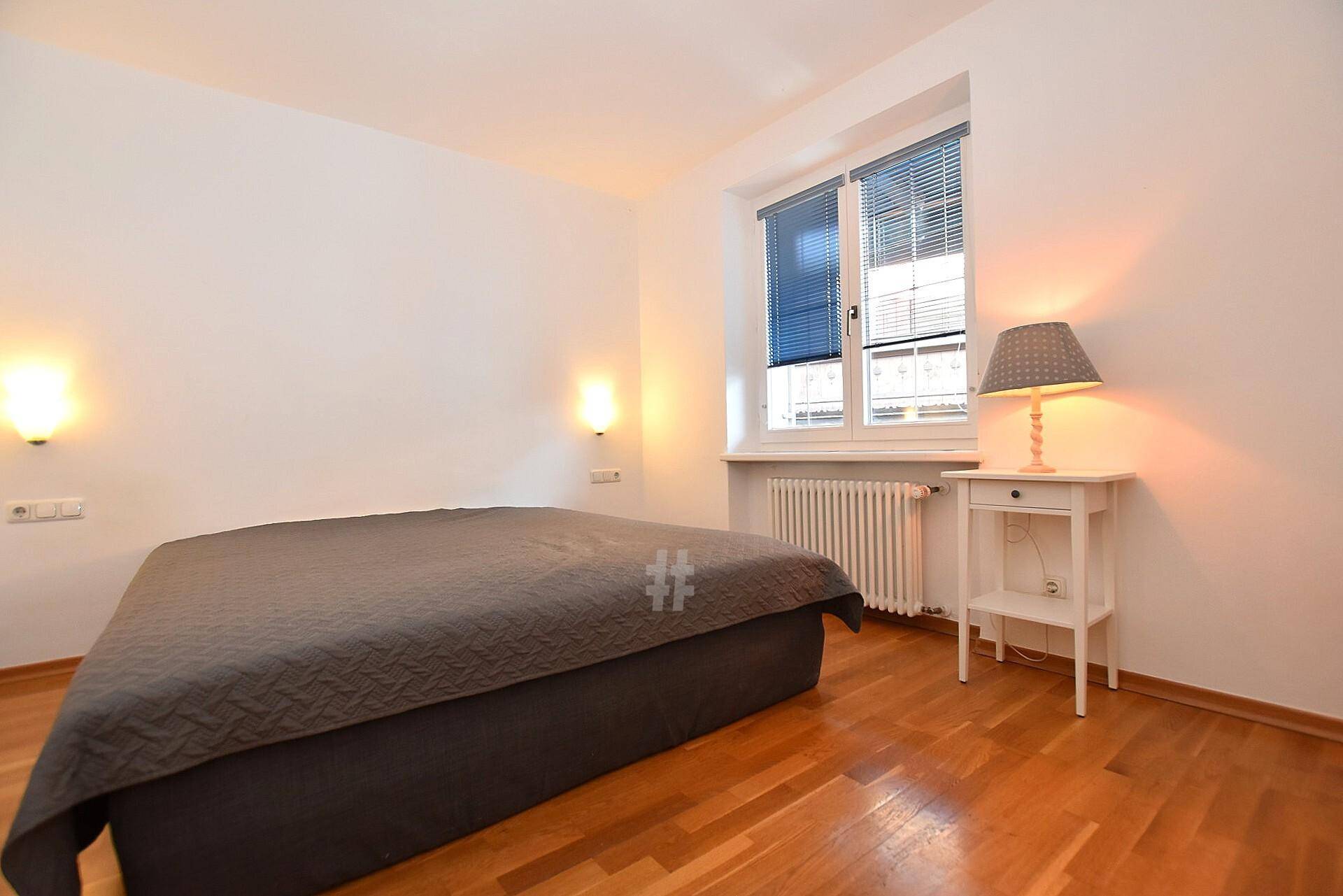 Gemütliches Schlafzimmer mit Holzboden, einem Doppelbett und einem Fenster mit Jalousien für Privatsphäre.