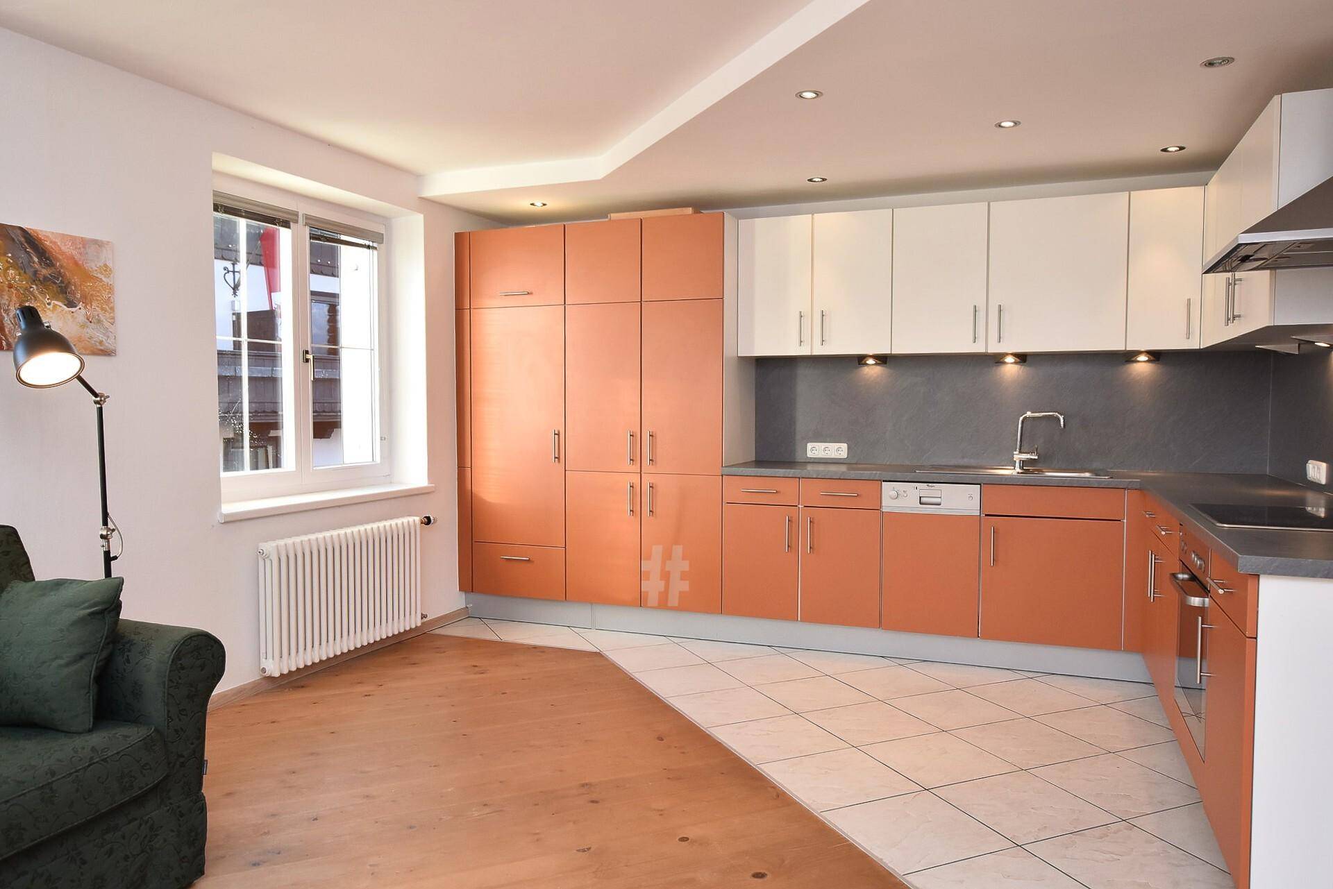 Moderne Küche mit orangefarbenen und weißen Schränken, integrierten Geräten und Fliesenboden.