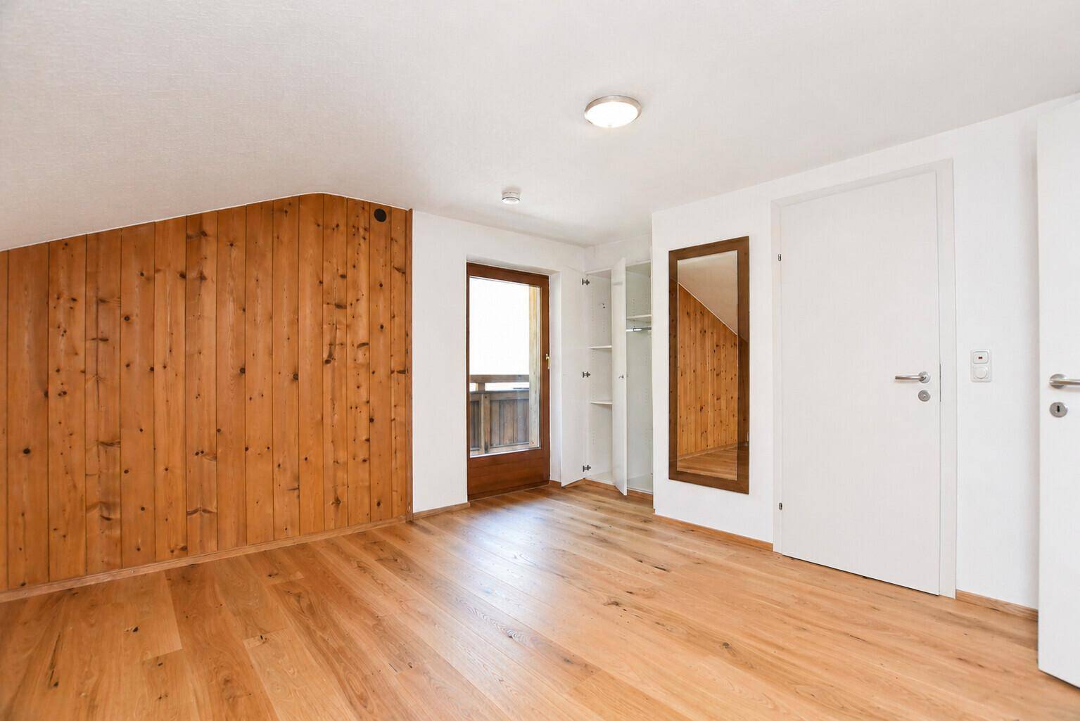 Gemütliches Schlafzimmer mit Holzboden, Holzwandverkleidung und integriertem Kleiderschrank sowie Balkonzugang.