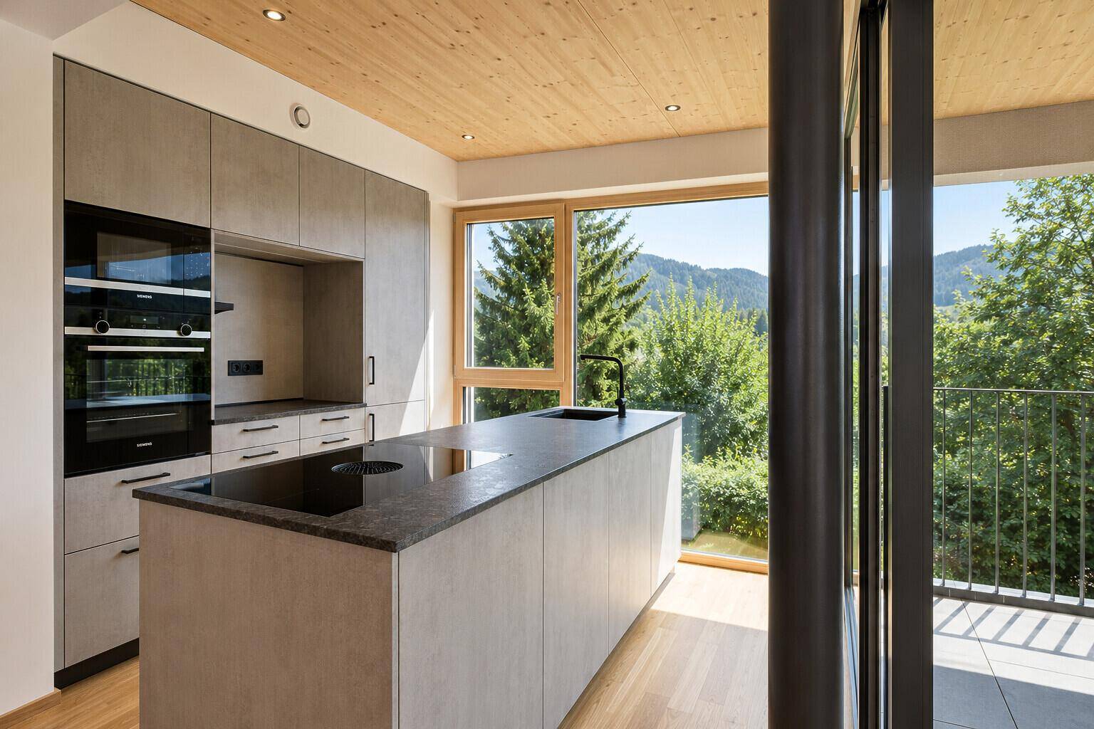 Helle, moderne Küche mit Kochinsel, dunkler Arbeitsplatte und weitem Blick in die Natur.