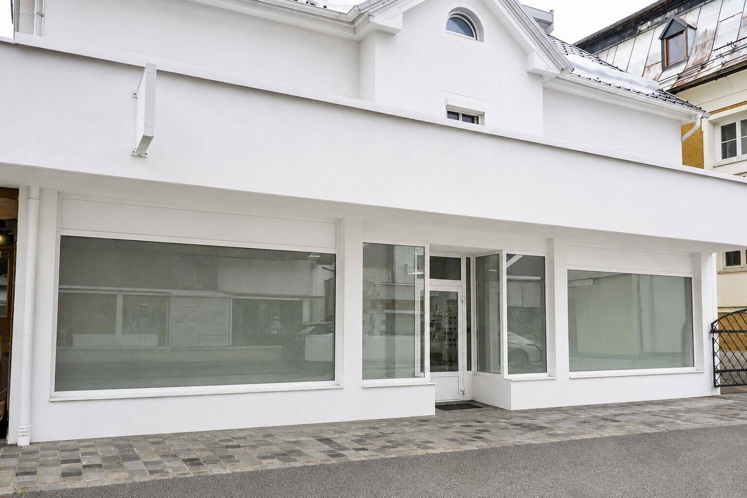 Moderne Geschäftsfassade mit großen Schaufenstern und weißem Putz.