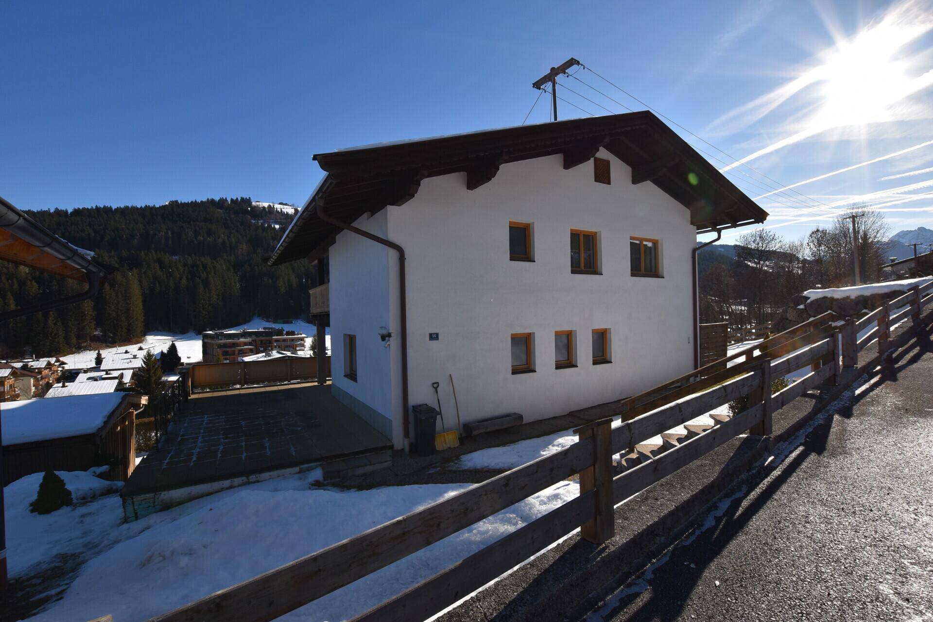 Rückseite des Hauses mit gepflastertem Bereich und Holzzaun in einer sonnigen Winterlandschaft.
