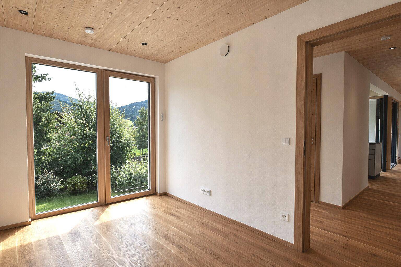 Helles Schlafzimmer mit Holzboden, Holzdecke und Blick auf den gepflegten Garten.