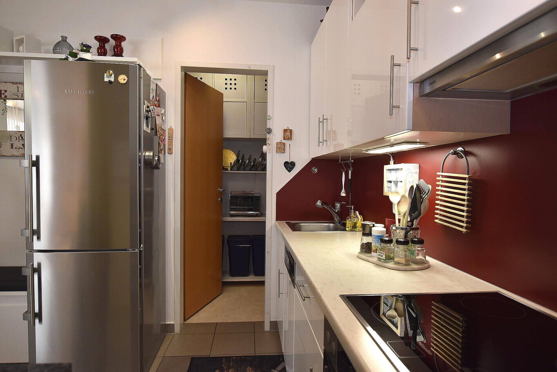 Moderne Küche mit weißen Hochglanzschränken, roter Rückwand und integriertem Kühlschrank.