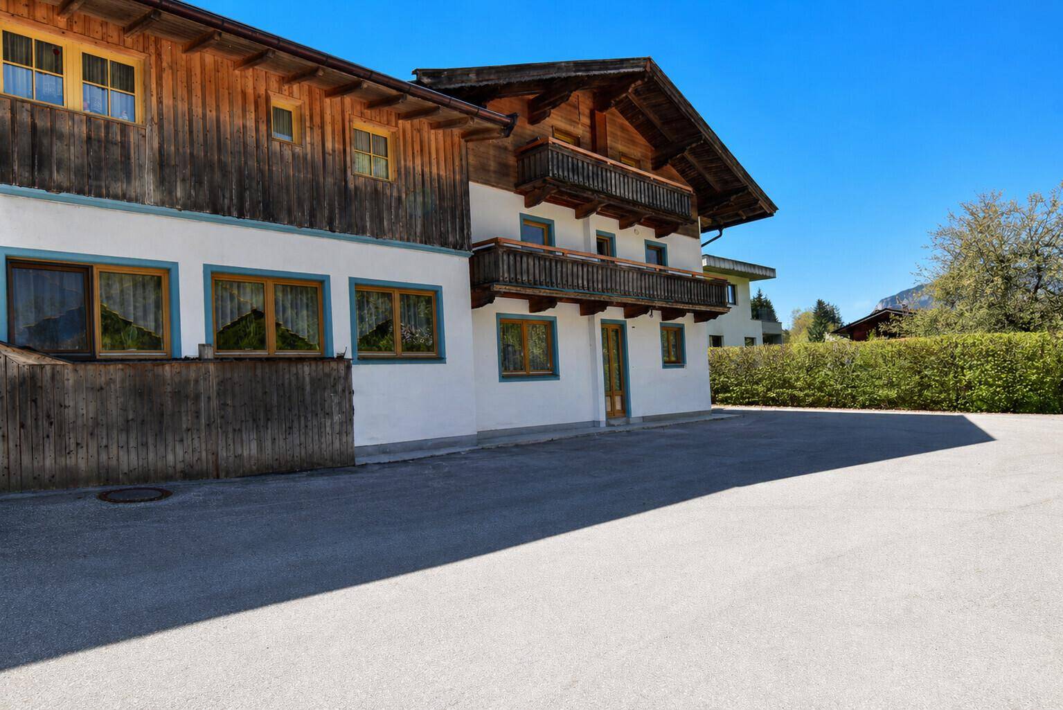 Traditionelles Alpenhaus mit Holzfassade, Balkonen und großzügiger gepflasterter Fläche davor.
