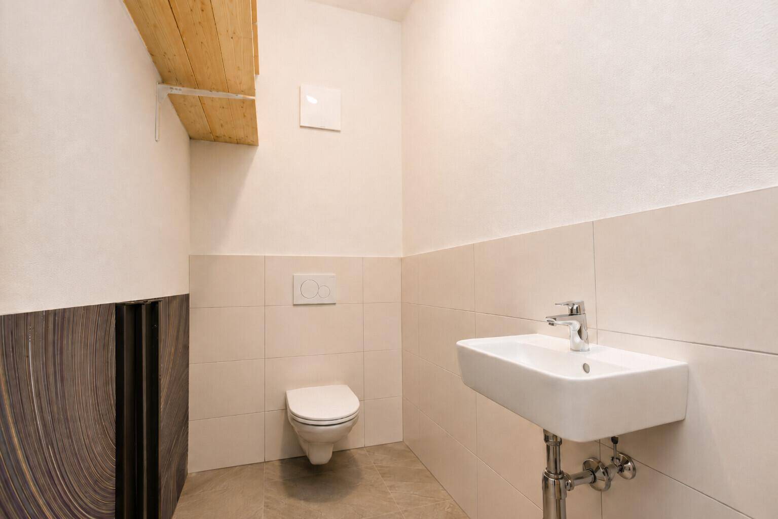 Modernes Gäste-WC mit wandhängender Toilette und kleinem Waschbecken, in hellen Fliesen gehalten.