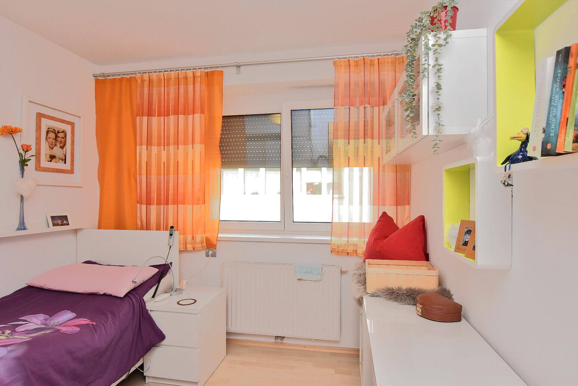 Kinderzimmer oder Gästezimmer mit Einzelbett, bunten Vorhängen und Fenster mit Rollladen.