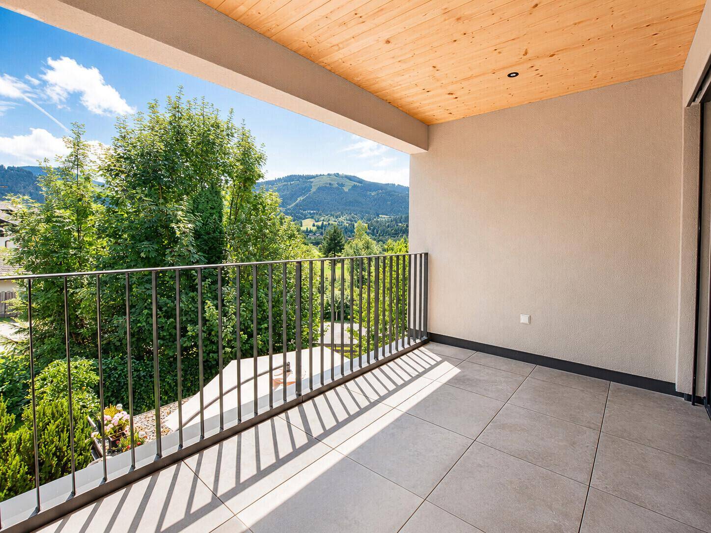 Geräumiger Balkon mit Fliesenboden, Holzdecke und weitem Blick auf die Berglandschaft.