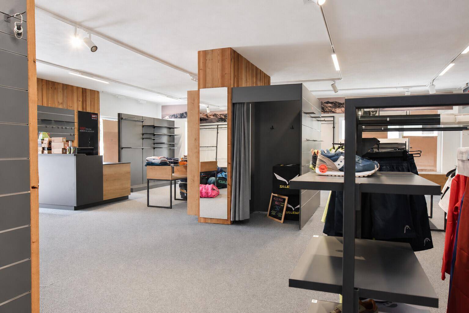 Geräumiger Verkaufsraum mit Regalen, Umkleidekabine und Kassentheke, ideal für Sport- oder Outdoor-Bekleidung.