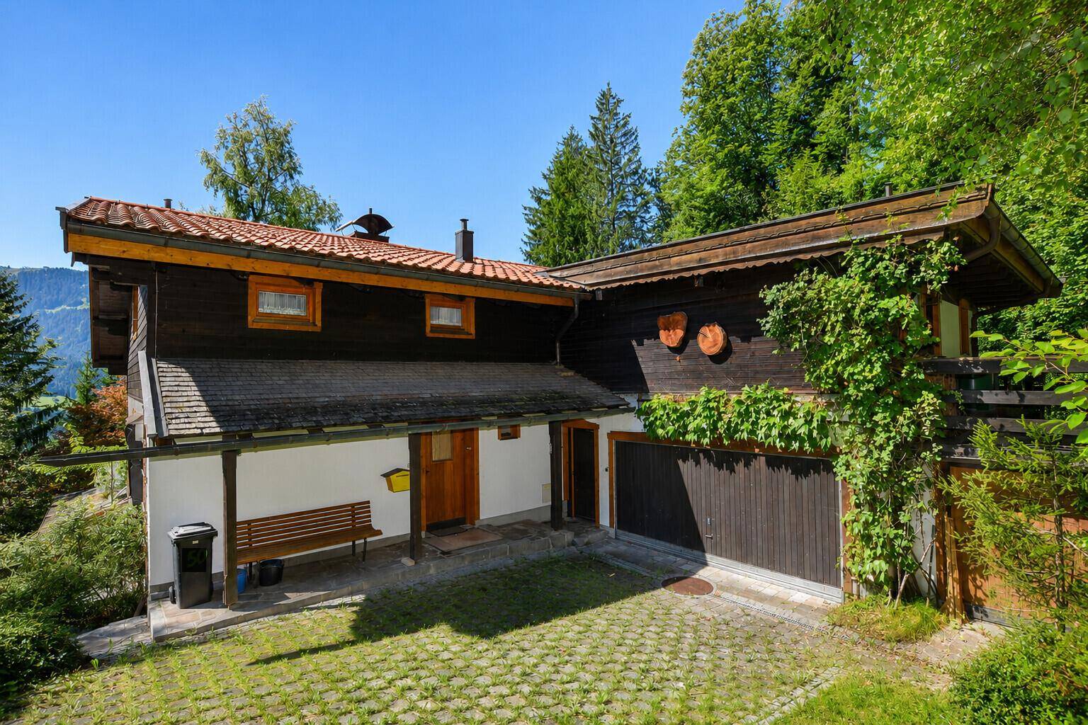 Traditionelles Haus mit Holzfassade, gepflastertem Eingangsbereich und integrierter Garage.