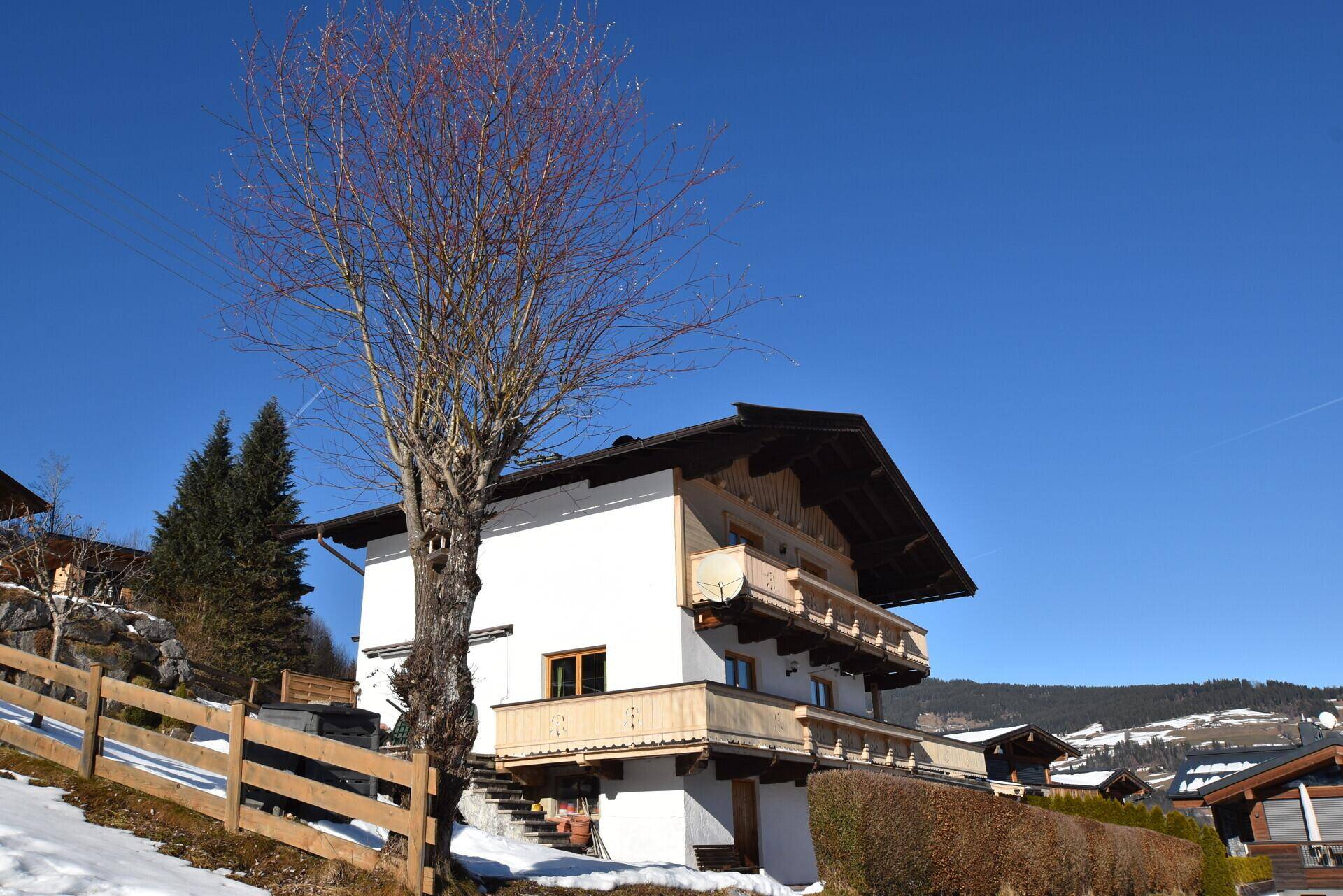 Alpines Haus mit Holzbalkonen und weißer Fassade, umgeben von Schnee und Bäumen.