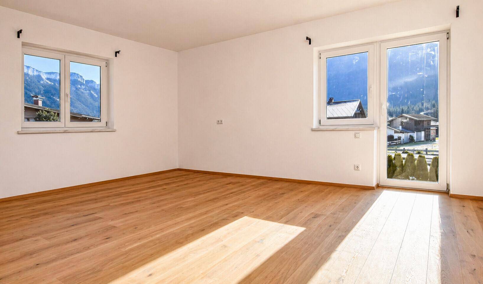 Lichtdurchfluteter Raum mit Holzboden und weitem Bergblick durch die Fenster.