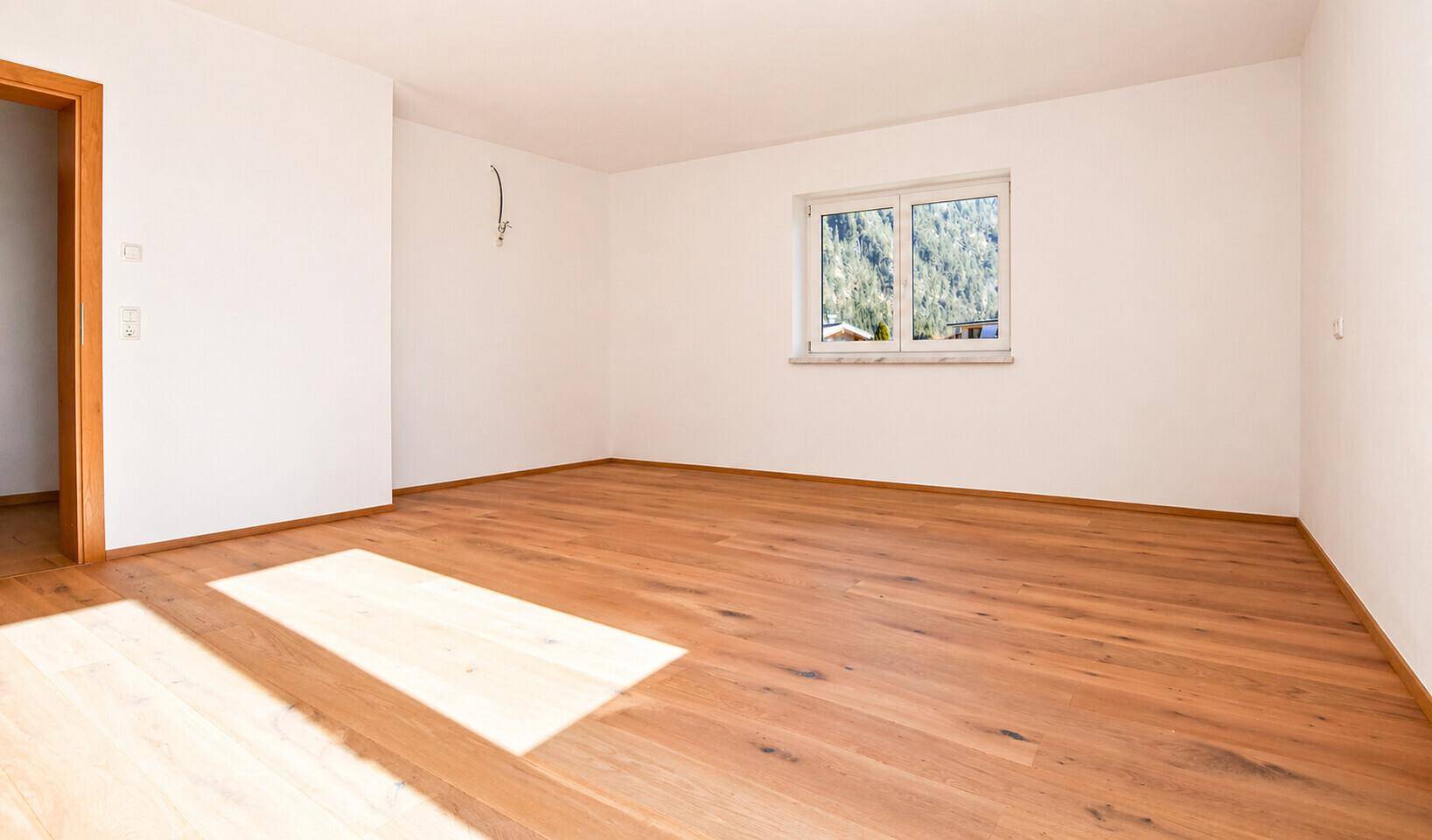 Geräumiges Schlafzimmer mit Holzboden und Fensterblick auf die Berge.