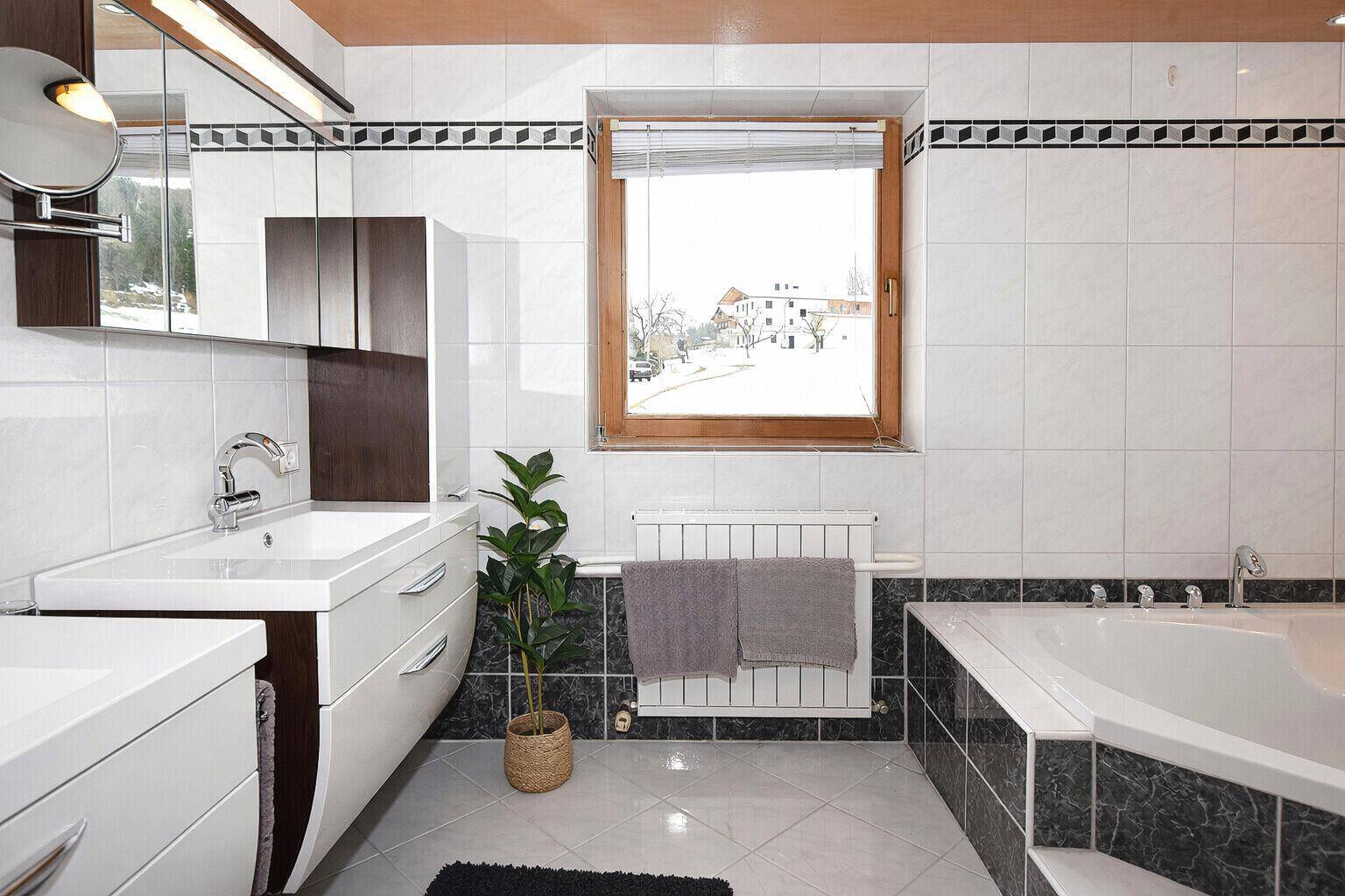 Badezimmer mit Badewanne, Doppelwaschbecken und Fenster mit Blick nach draußen.