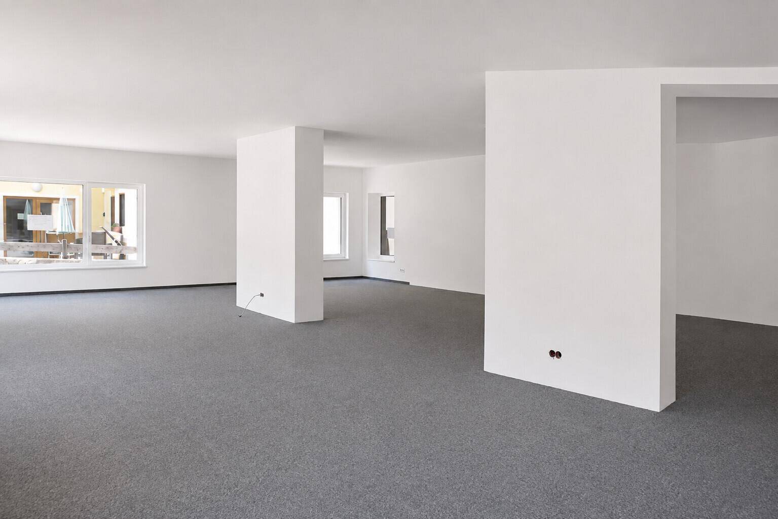 Großer, heller Gewerberaum mit Säulen und Teppichboden, bietet flexible Gestaltungsmöglichkeiten für verschiedene Nutzungen.