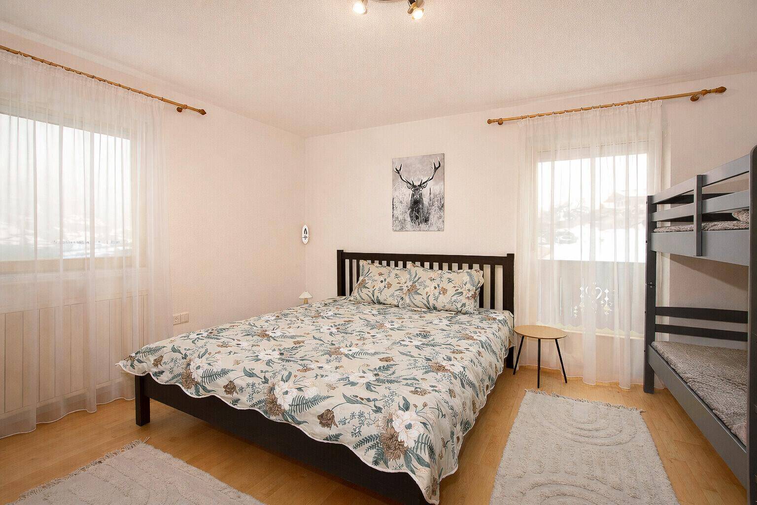 Geräumiges Schlafzimmer mit Doppelbett, Etagenbett und zwei Fenstern.
