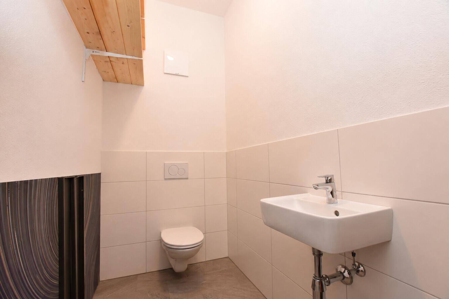 Modernes Gäste-WC mit wandhängender Toilette, rechteckigem Waschbecken und weißen Fliesen an den Wänden.