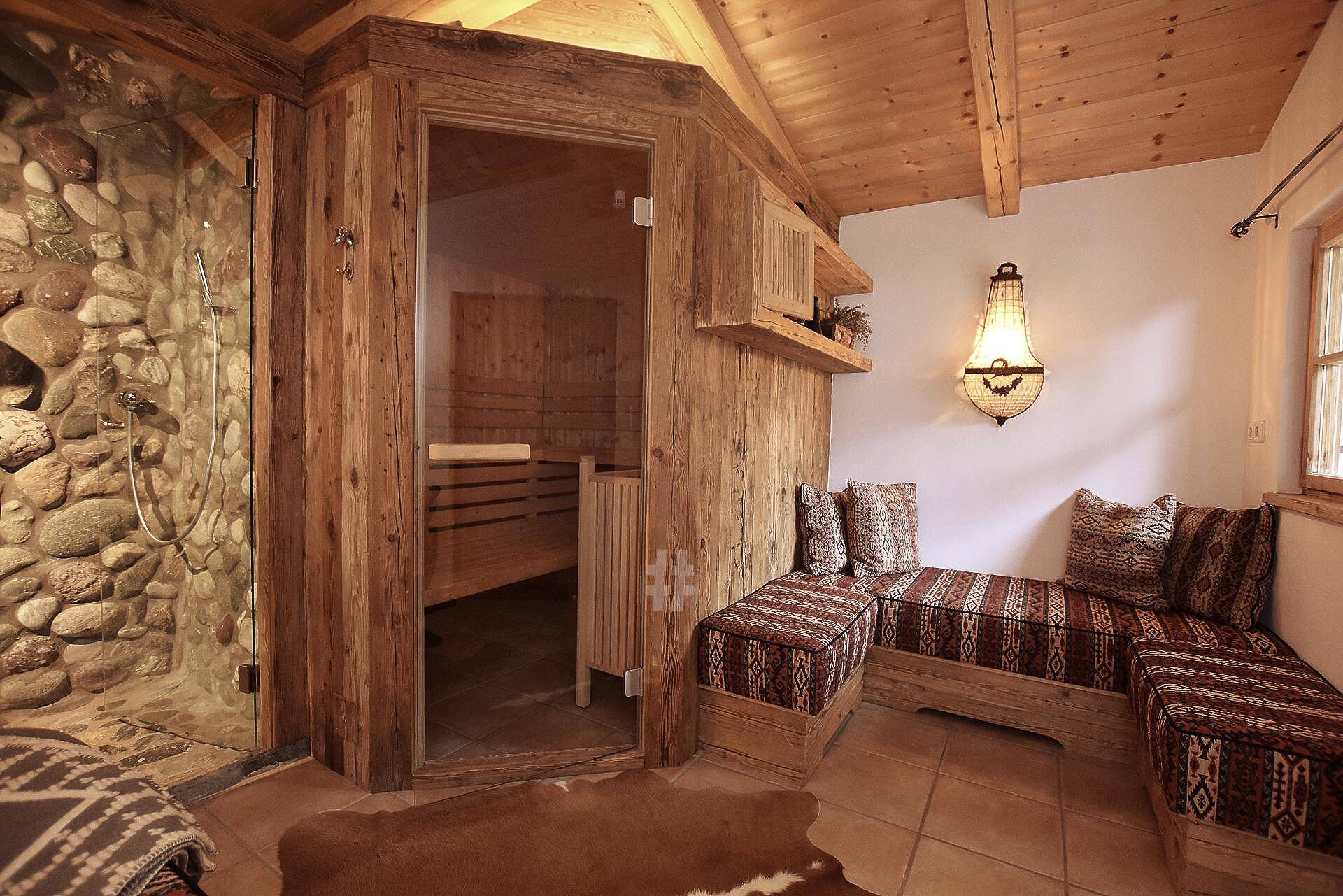 Geräumiger Wellnessbereich mit Holzsauna, Steindusche und bequemen Sitzbänken im Chalet-Stil.