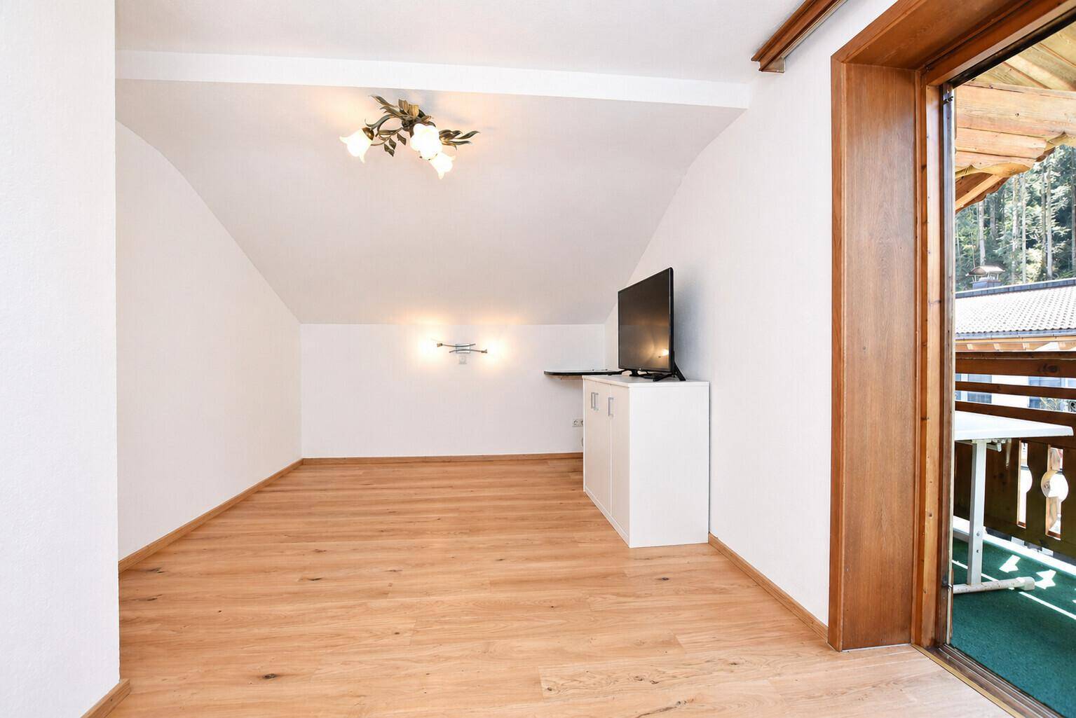 Helles Schlafzimmer mit Dachschräge, Holzboden und Zugang zu einem kleinen Balkon.
