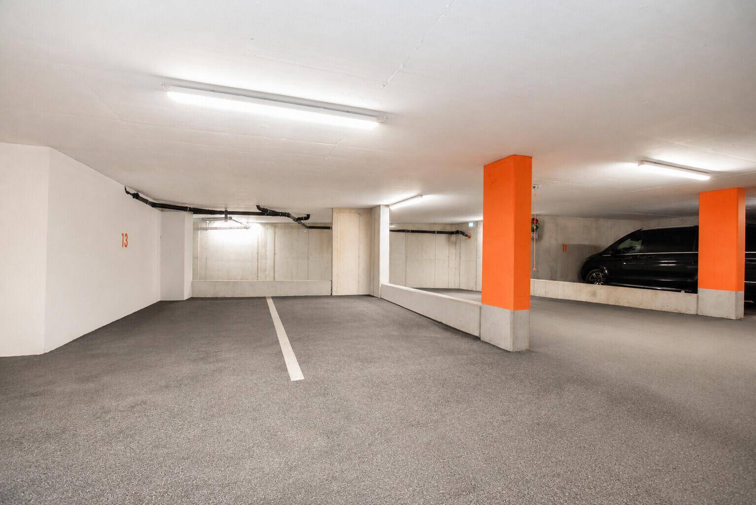 Geräumige Tiefgarage mit markierten Stellplätzen, Betonwänden und auffälligen orangefarbenen Säulen.