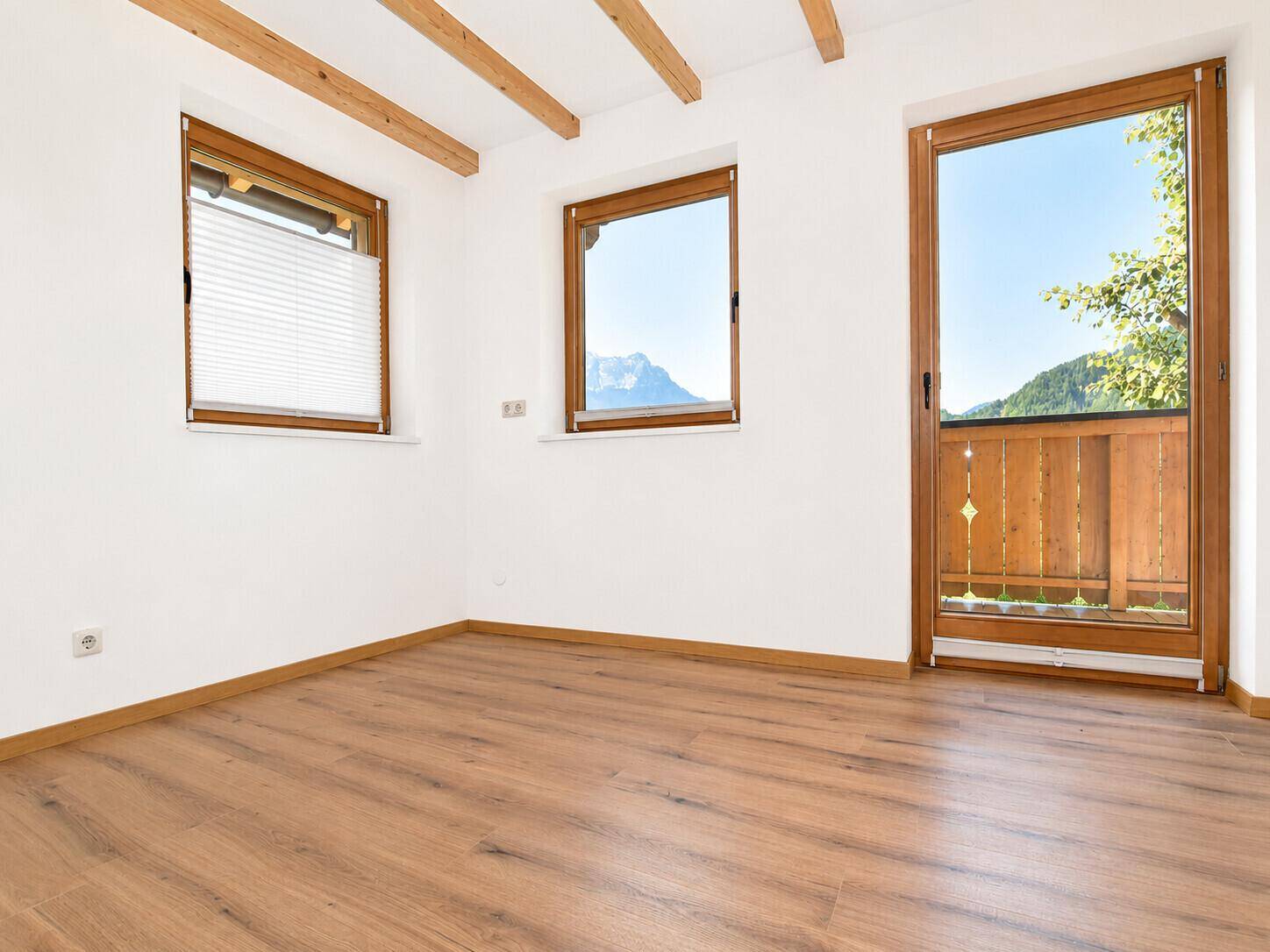 Helles Schlafzimmer mit Holzbalken, Holzboden und Bergblick vom Balkon.