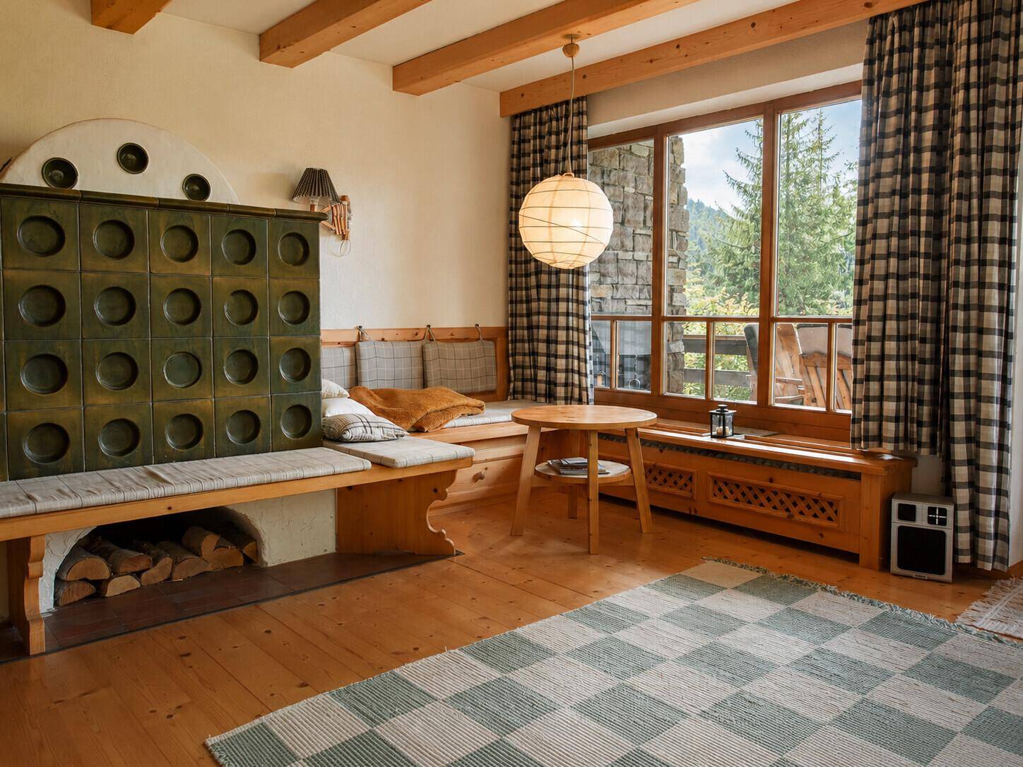 Rustikales Wohnzimmer mit Kachelofen, Holzbalken und großen Fenstern mit Waldblick.