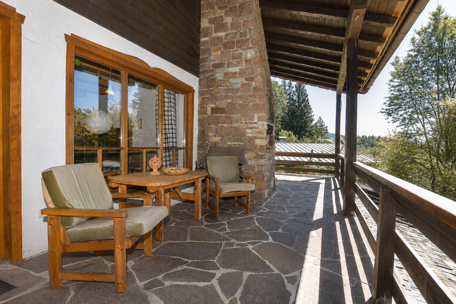 Gemütliche überdachte Terrasse mit Steinboden, Holztisch und Stühlen, ideal zum Entspannen.