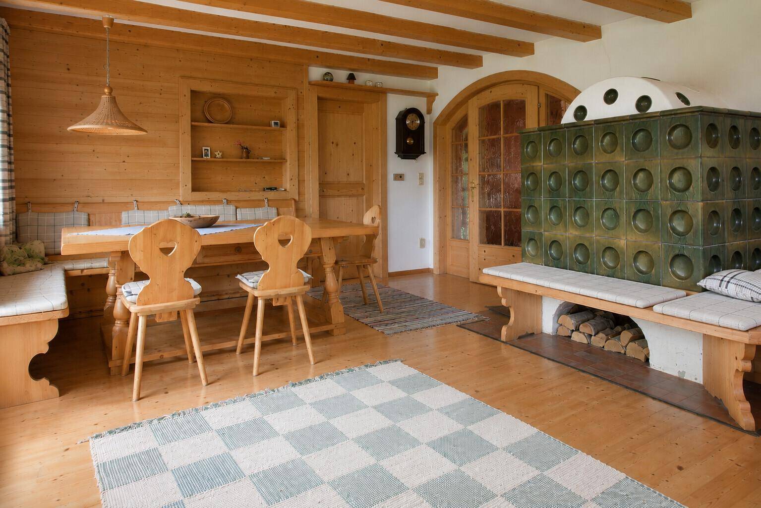 Gemütlicher Essbereich mit Holztisch, Stühlen und traditionellem Kachelofen in offenem Raum.