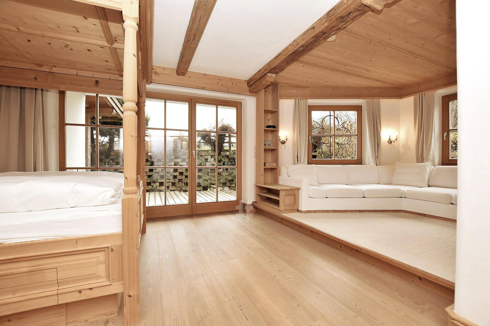 Helles Schlafzimmer im Chalet-Stil mit Holzbalken, großem Bett und Zugang zur Terrasse.