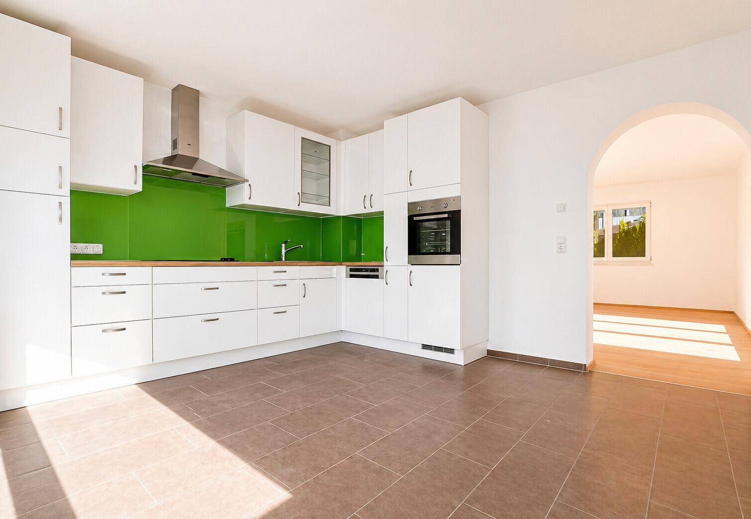 Moderne Küche mit weißen Hochglanzschränken, grüner Rückwand und Fliesenboden.
