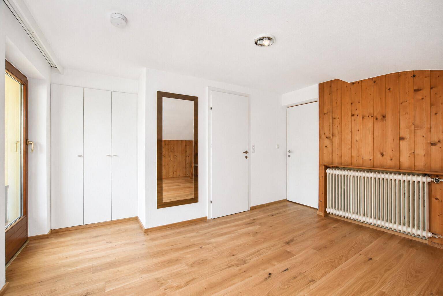 Helles Schlafzimmer mit Holzboden, Einbauschränken und traditioneller Holzverkleidung an einer Wand.