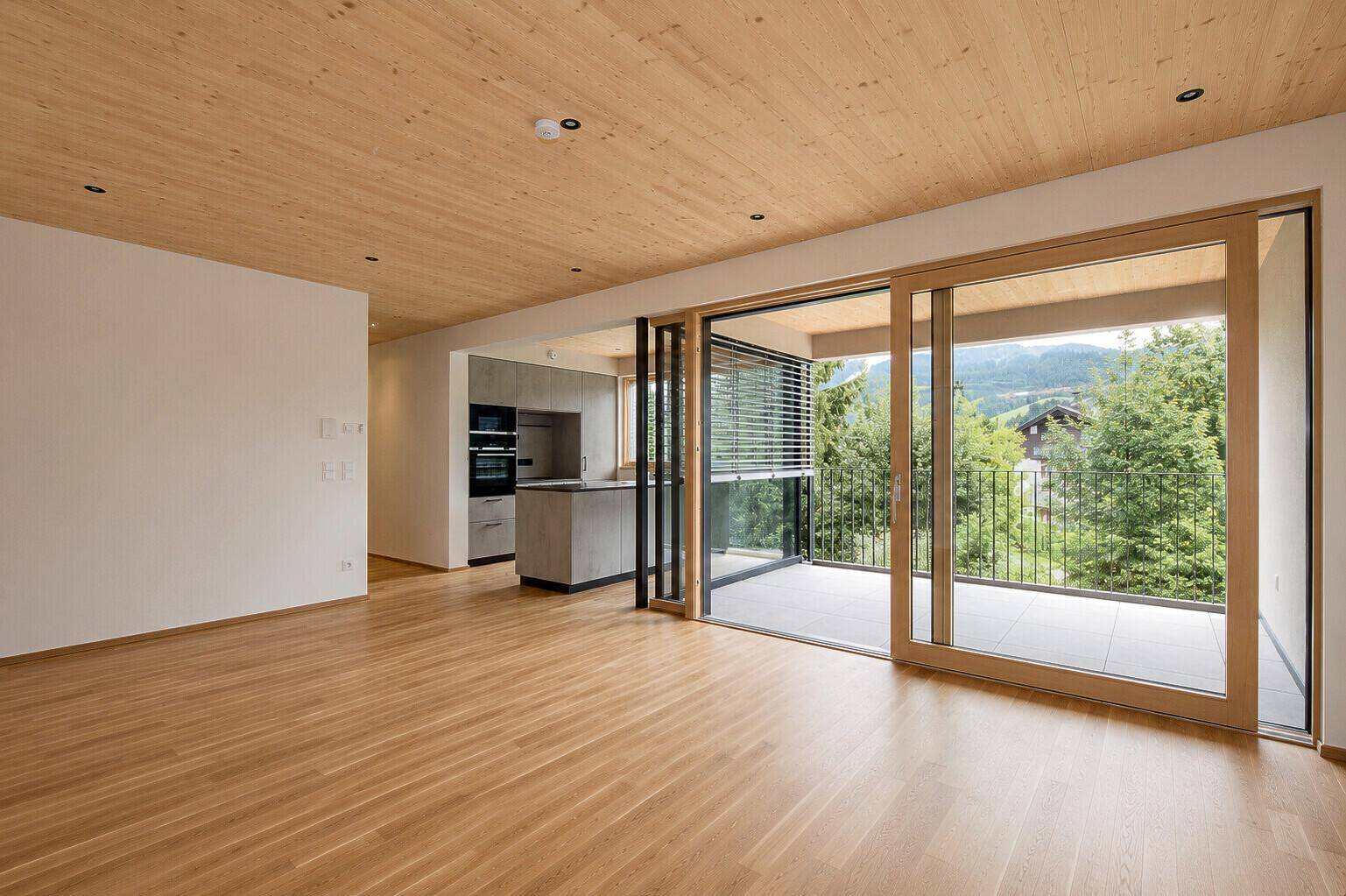 Geräumiger offener Wohnbereich mit Holzboden, Holzdecke und Blick auf die umliegende Berglandschaft.