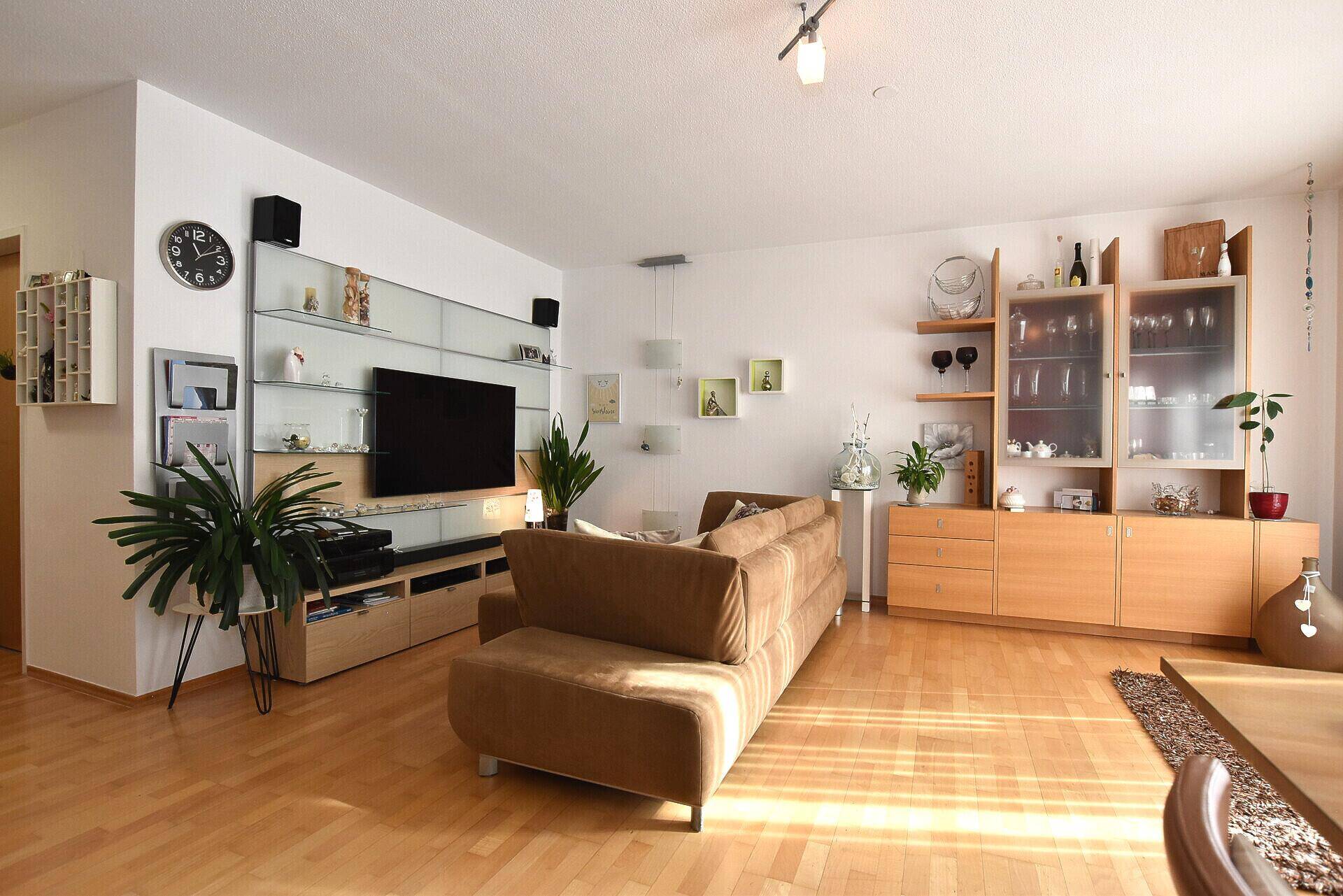 Geräumiges Wohnzimmer mit beigem Sofa, Holzboden und viel Stauraum in den Schränken.