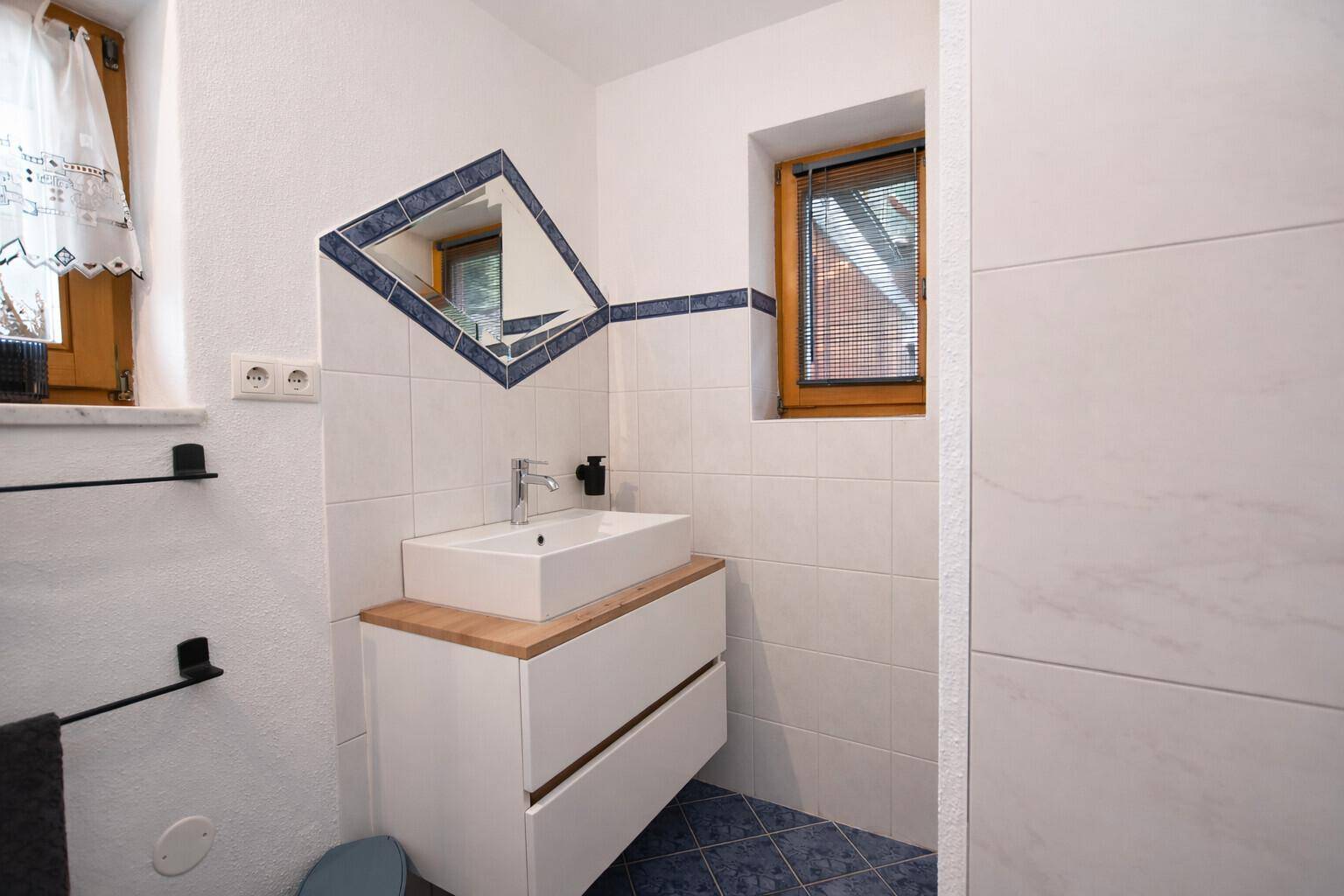 Modernes Badezimmer mit Einzelwaschbecken, Fenster und blauen Akzentfliesen.