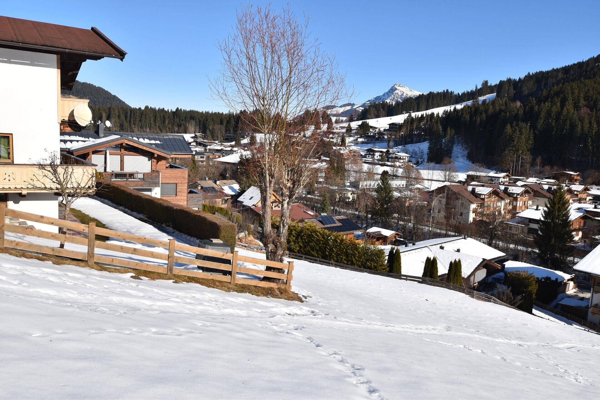 Weitläufige Winterlandschaft mit verschneiten Dächern und Bergen im Hintergrund unter blauem Himmel.
