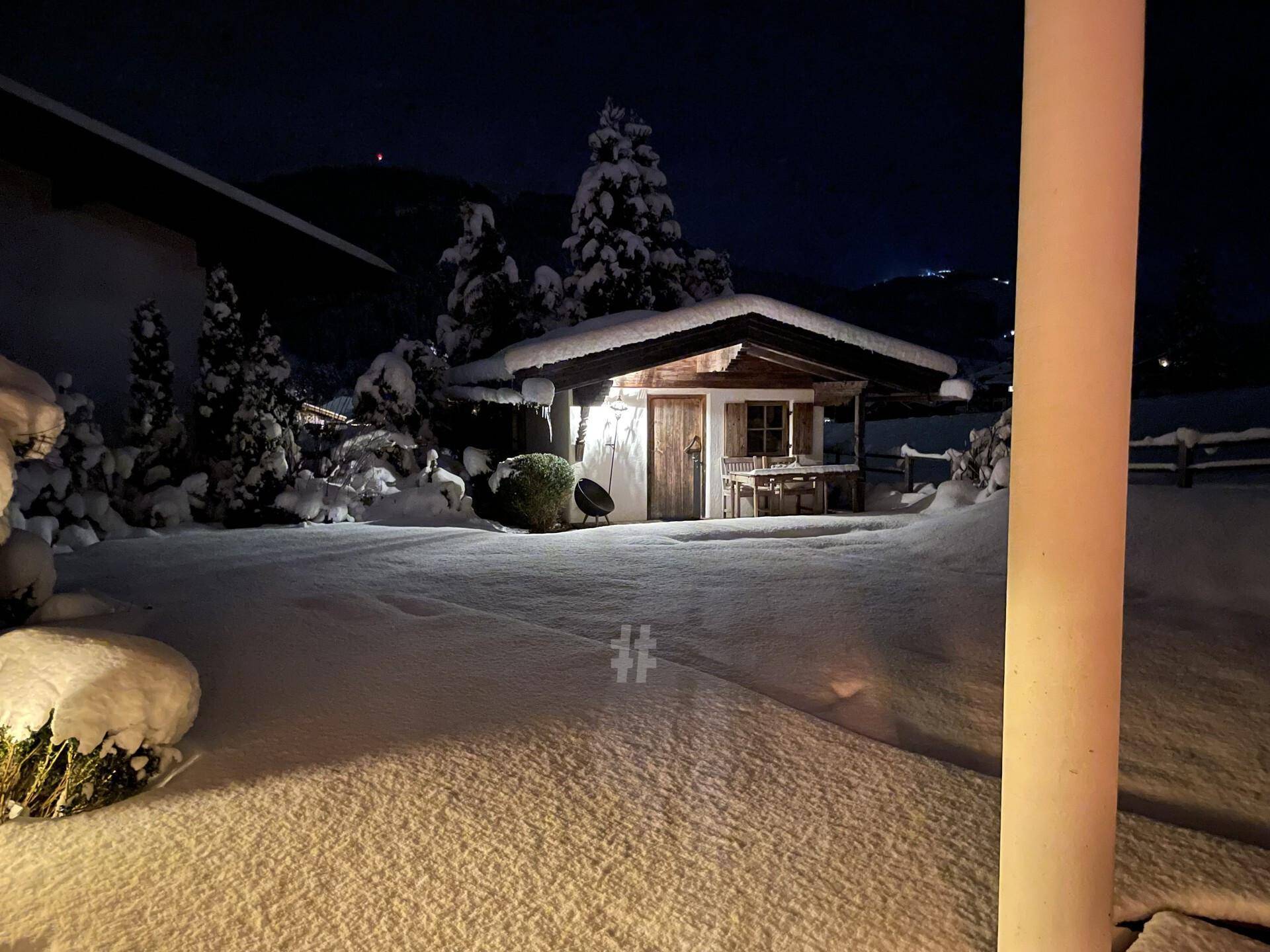 Verschneite Gartenhütte im Winter bei Nacht, umgeben von einer idyllischen Schneelandschaft.